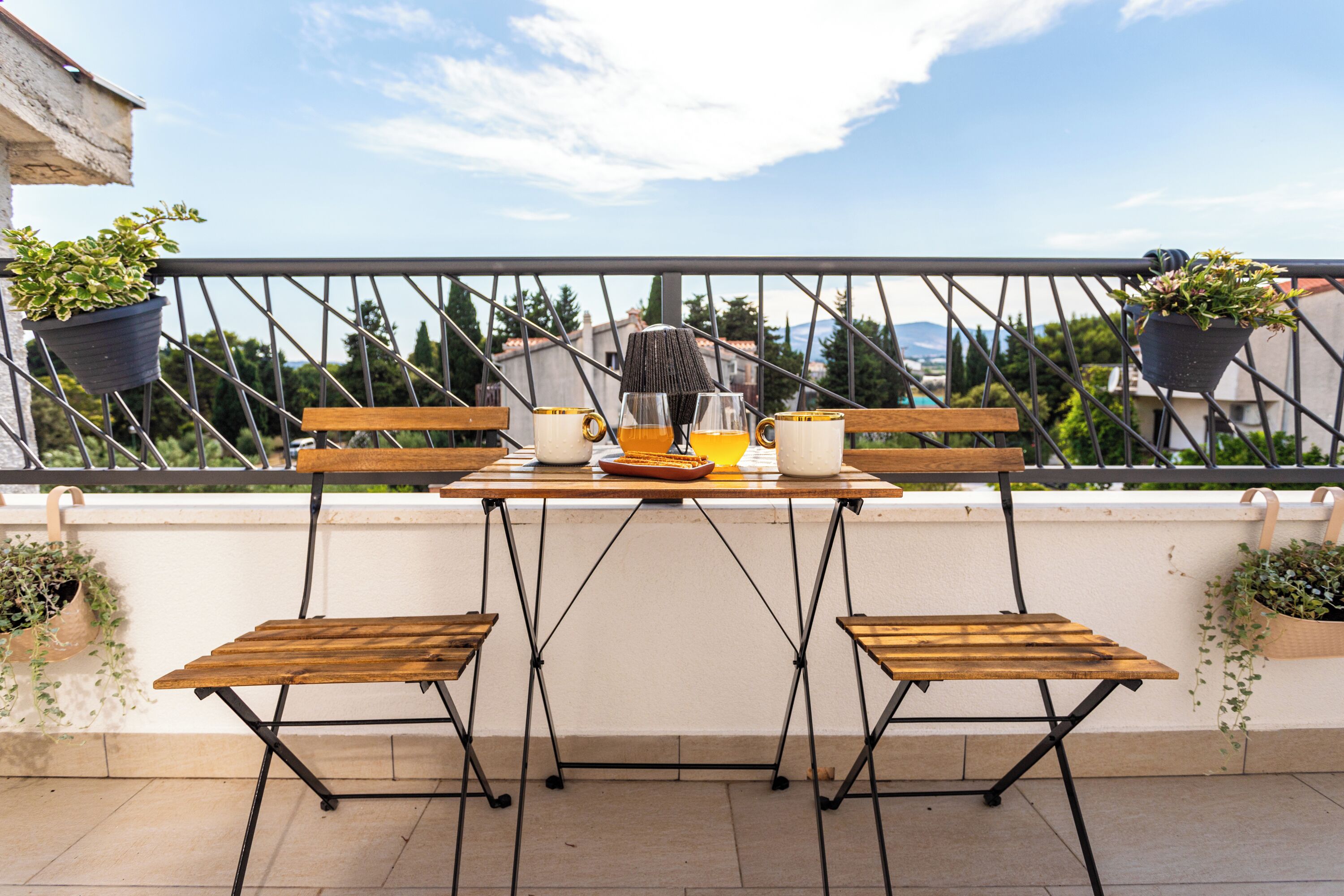 Een balkon met een houten tafel en stoelen, plantenbakken en uitzicht op de stads panorama.