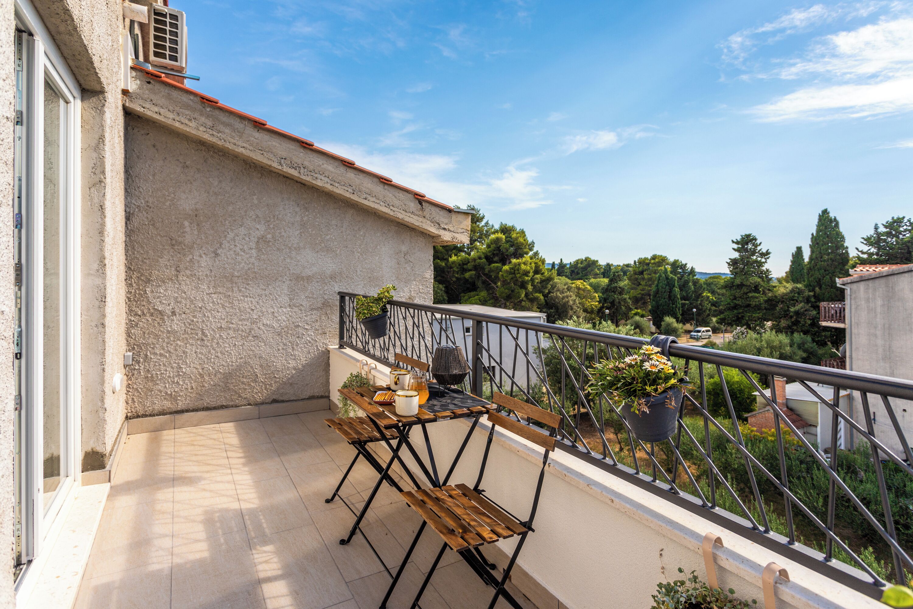 A balcony with a table, chairs, and potted plants.