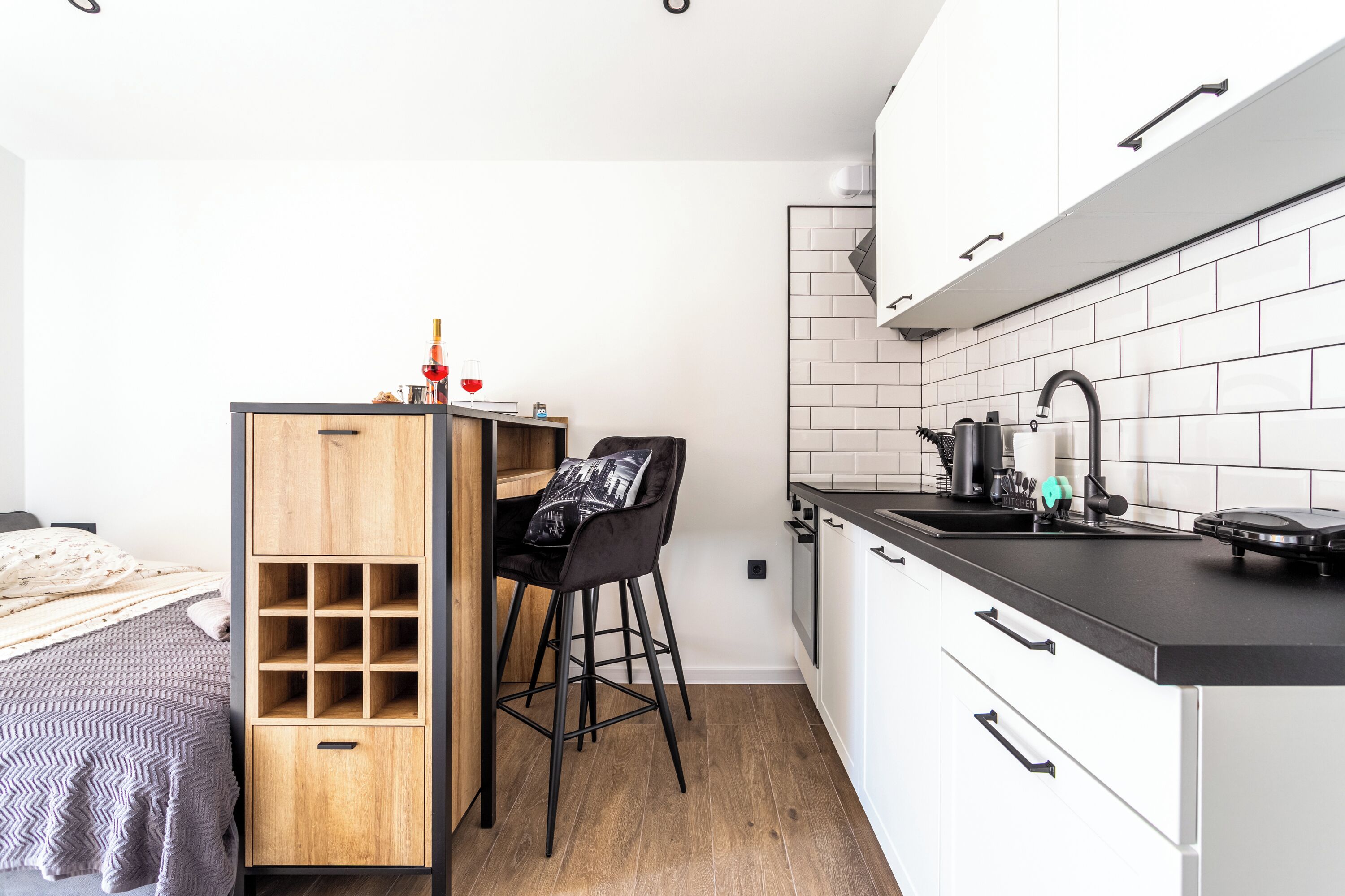 Een compacte keuken met een houten barstoel, een kleine eettafel en een zwart aanrecht.