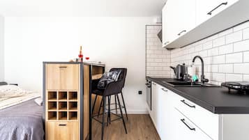 Een compacte keuken met een houten barstoel, een kleine eettafel en een zwart aanrecht.
