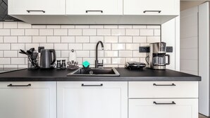 Una cocina moderna con armarios blancos, encimera negra, pileta de acero inoxidable y cafetera.