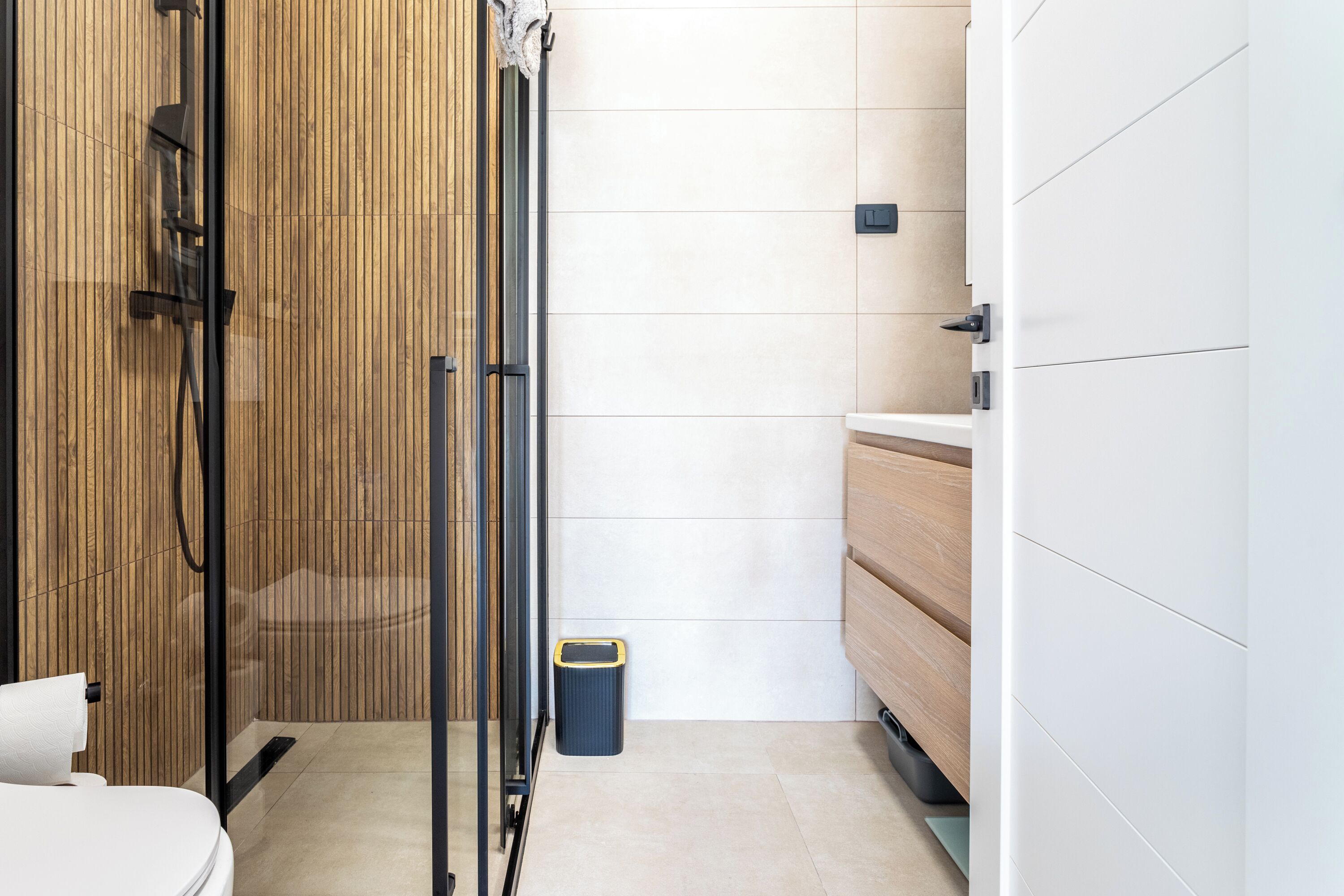 A modern bathroom with a glass shower enclosure, a toilet, and a trash bin.
