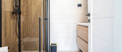 A modern bathroom with a glass shower enclosure, a toilet, and a trash bin.