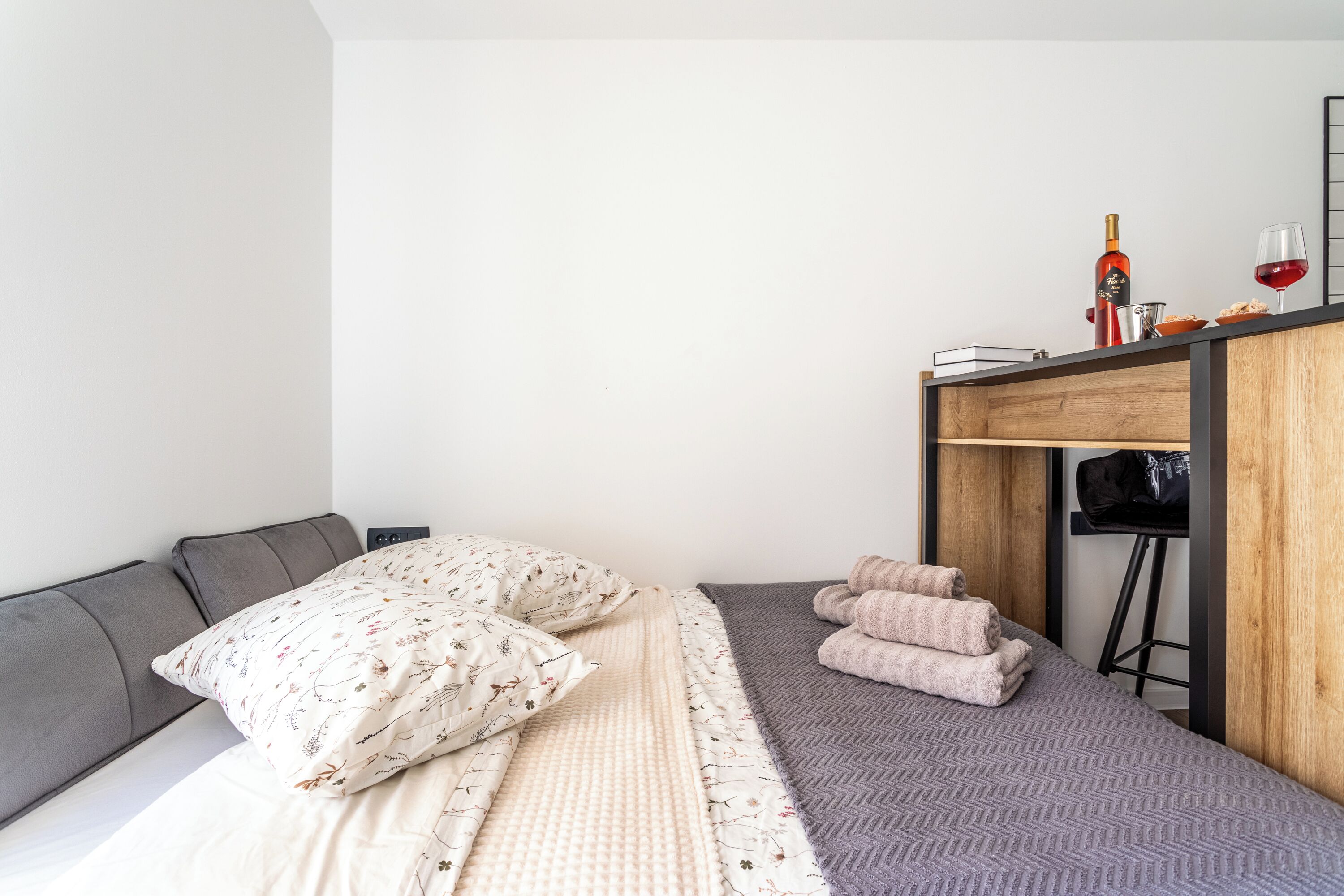 Une chambre à coucher de taille réduite, comprenant un lit, des oreillers, une petite table avec une bouteille et un verre, et une chaise.