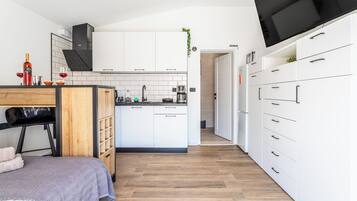 A modern kitchen with white cabinets, a wooden countertop, and a black TV mounted on the wall.