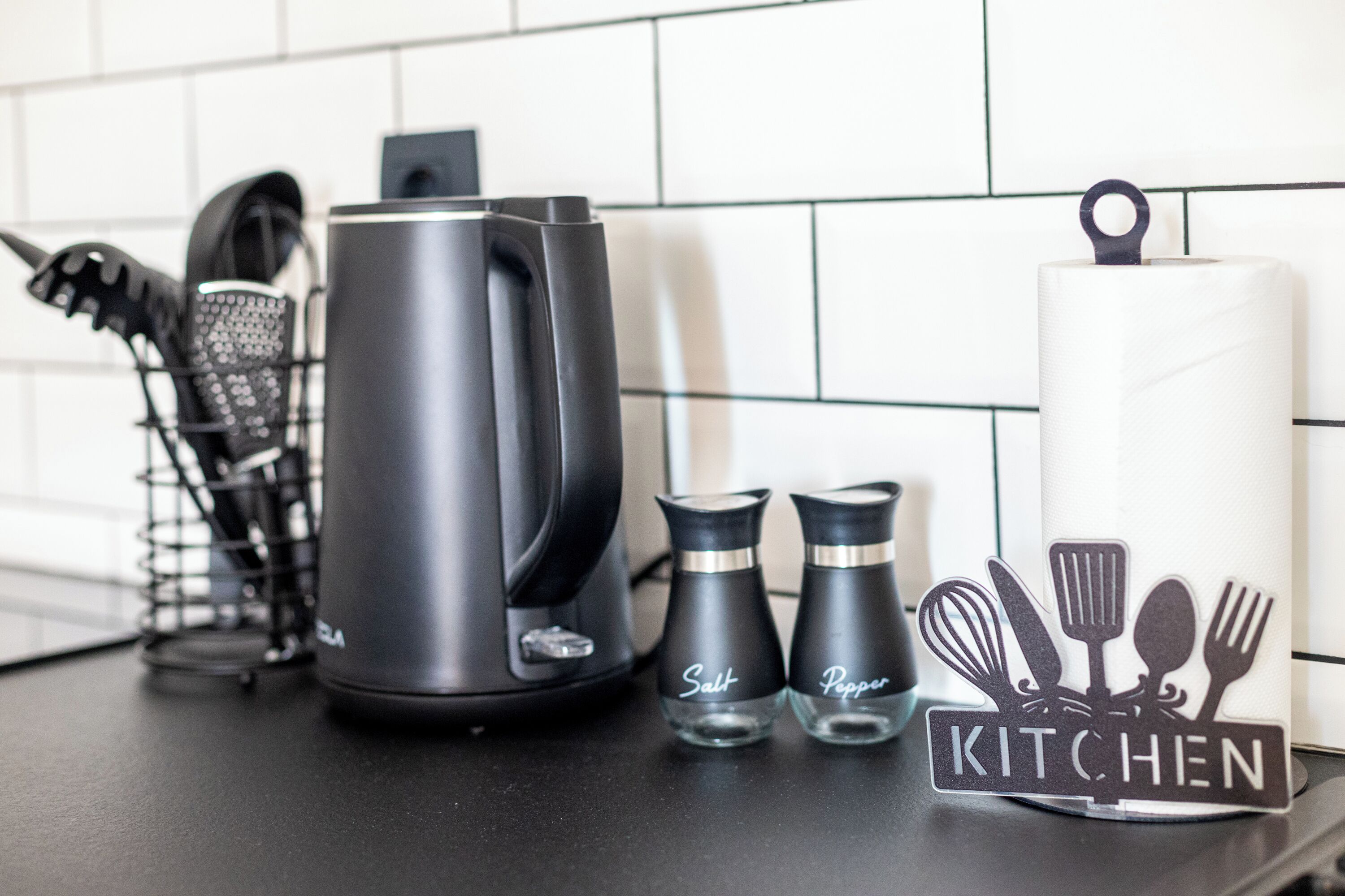 A kitchen counter with a kettle, salt and pepper shakers, a whisk, and a spatula on a tray.