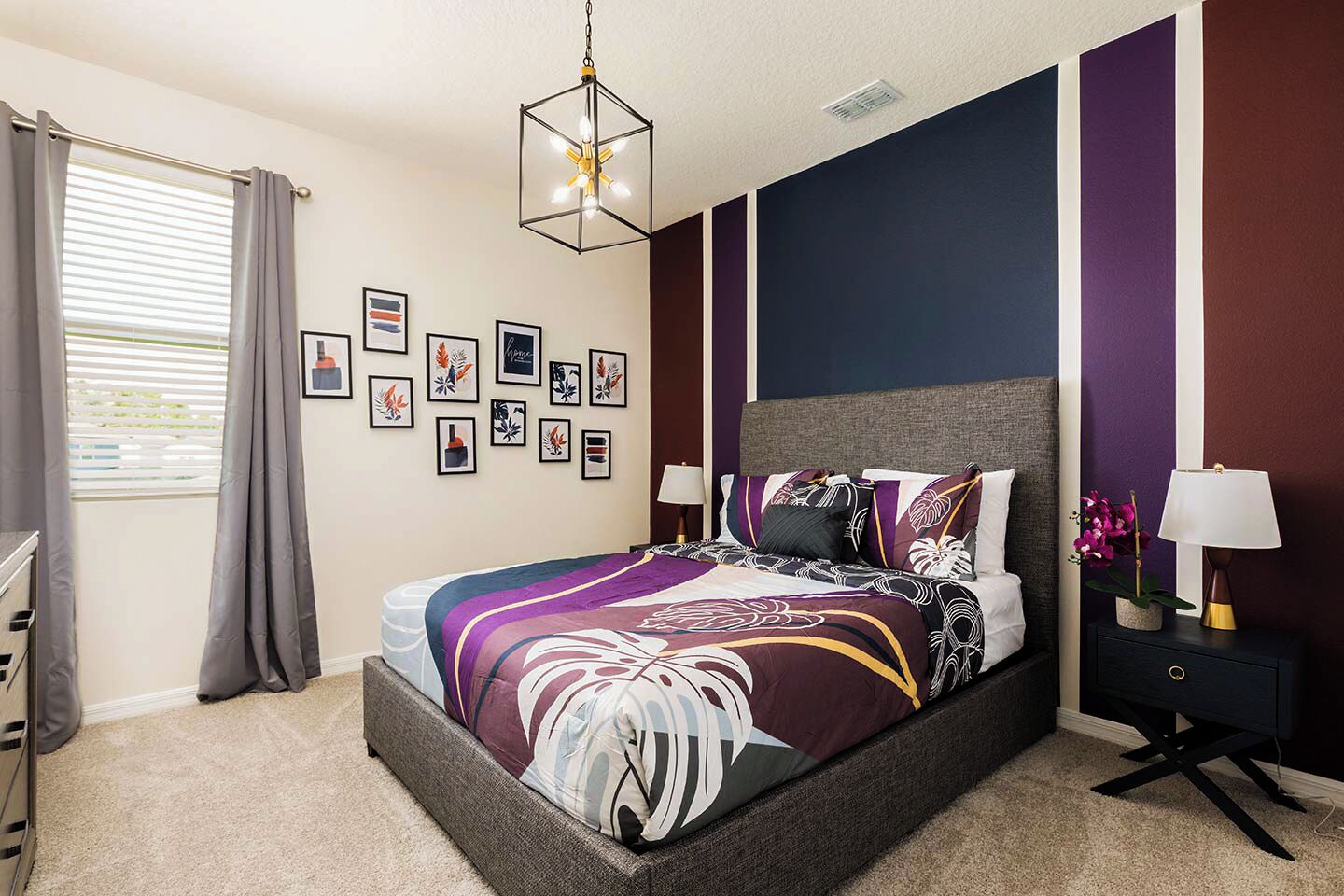A bedroom with a bed, a nightstand, a lamp, a window with curtains, and wall art.