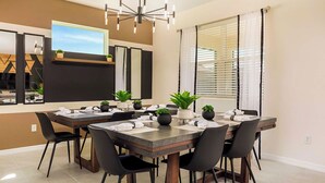 A modern dining area with a long table, black chairs, and potted plants. - 8904-TropicalHaven (Kissimmee)