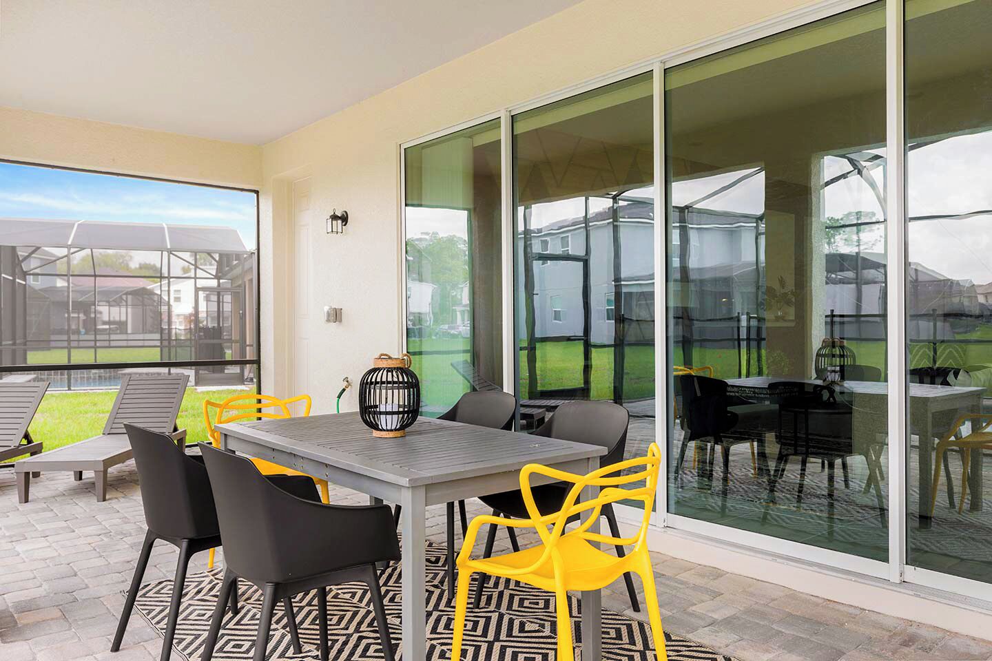 A patio area with a table and chairs, a lantern, and a view through large glass doors.