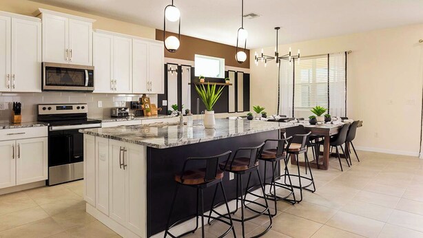 A modern kitchen with white cabinets, a central island with bar stools, a microwave, an oven, and pendant lighting. - 8904-TropicalHaven (Kissimmee)