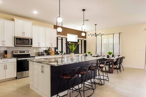 Una cocina moderna con armarios blancos, una isla central con taburetes, microondas, horno e iluminación colgante.