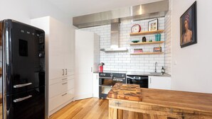 Una cocina moderna con armarios blancos, un refrigerador negro, piso de madera y una campana extractora de acero inoxidable.