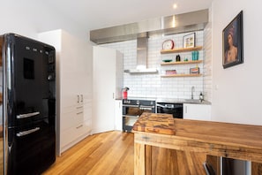 A modern kitchen with white cabinets, a black refrigerator, wooden flooring, and a stainless steel range hood. - Stylish 3BDR Unit in the Heart of Melbourne CBD (Melbourne)