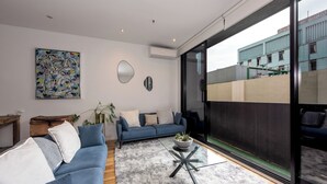 Una sala de estar moderna con un sofá azul, una mesa de centro de vidrio y un amplio ventanal con vistas a un edificio.