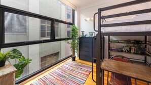 Una habitación pequeña con una cama litera, un escritorio, una estantería y una planta en maceta.