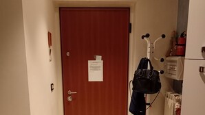 Un passadís amb una porta de fusta, un radiador, un safataixa vermella i un arbre per a gat.
