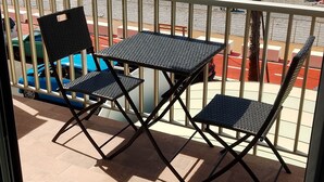 Un balcó amb dues cadires i una taula, amb vista a una platja on hi ha gent i una palmera.