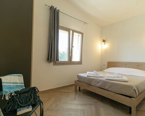 Een slaapkamer met een bed, een stoel, een handtas en een raam met gordijnen.