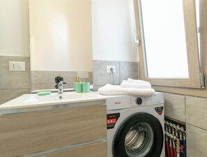 A modern bathroom with a sink, mirror, and a washing machine. - Villa Su Entu | with Garden close to the beach (Lanusei)