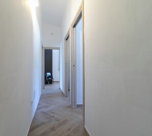 A narrow hallway with wooden flooring, white walls, and a door leading to another room. - Villa Su Entu | with Garden close to the beach (Lanusei)