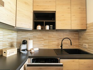A modern kitchen with wooden cabinets, a black countertop, a coffee machine, a sink, and a dish drying rack. - Villa Su Entu | with Garden close to the beach (Lanusei)