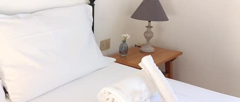Ein ordentlich gemachtes Bett mit weißen Leinentüchern, ein Nachttisch aus Holz mit einer Lampe und eine Vase mit Blumen.