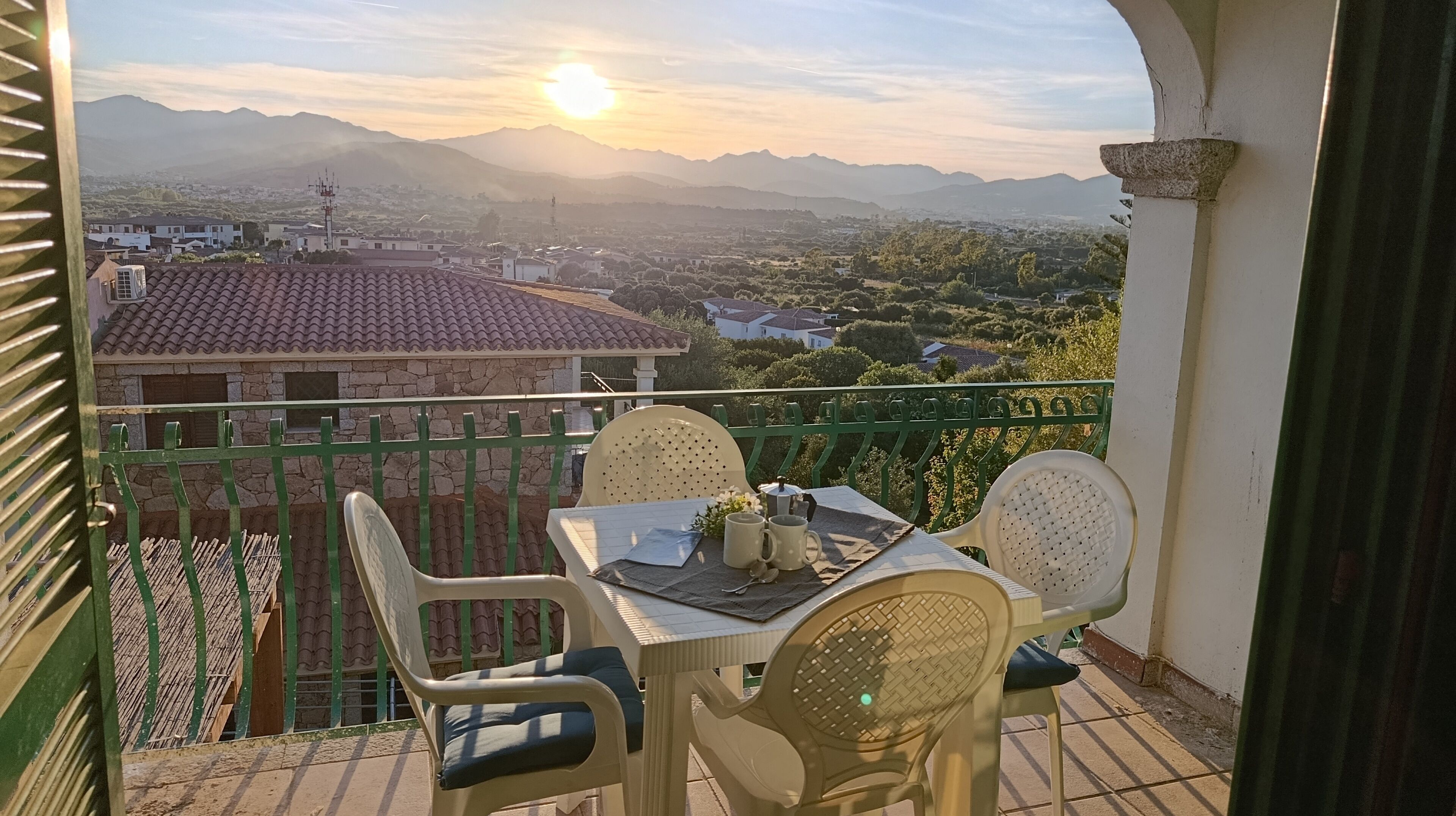 A balcony with a table, chairs, and a view of a town and mountains.