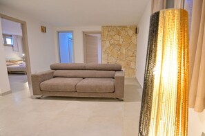 A living room with a sofa, a stone wall, and a door. - Villa Belvedere with private Pool in Castiadas (San Nicolo' Gerrei)