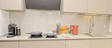 Eine moderne Küche mit Einbauherd, einer Kaffeemaschine, einem Wasserkocher und einem Spülbecken.