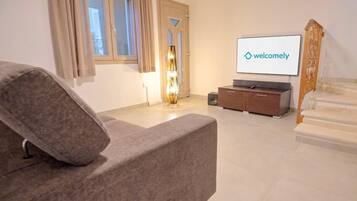 Un salon moderne avec un canapé, un téléviseur affichant un message de bienvenue, un escalier et une lampe.