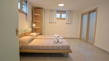 Habitación de hotel con dos camas, cabecero de madera, ventana con cortinas y puerta corrediza.