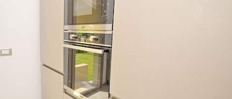 A kitchen with a built-in microwave and oven, a window, and a door leading to an outdoor area.