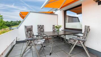 A rooftop terrace with a table and chairs, a window, and a view of the sky.