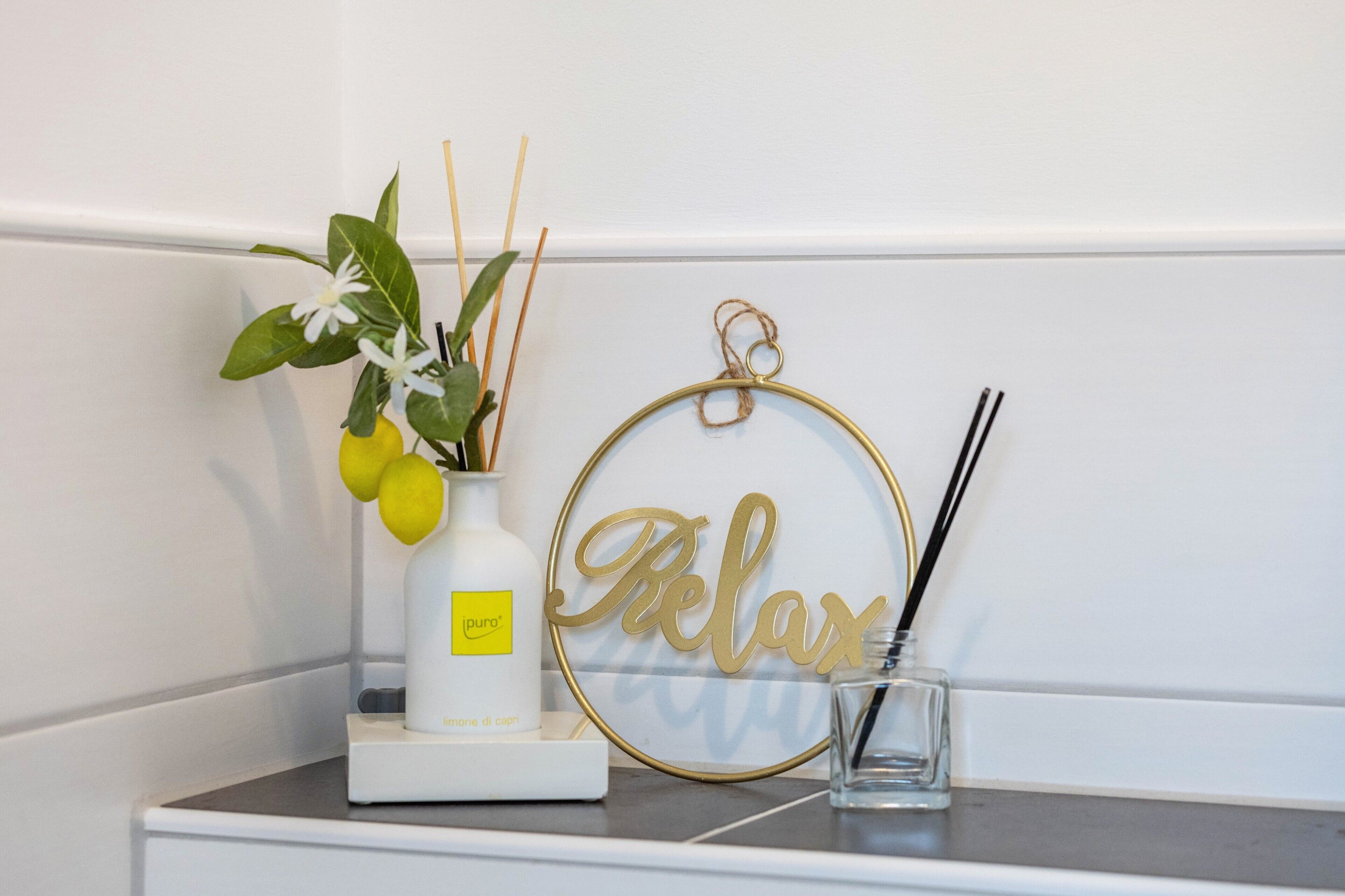 Estante blanco con una botella blanca, un vaso y un cartel dorado que dice 'Relax'.