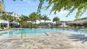 A swimming pool with lounge chairs, palm trees, and a building with balconies.