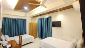 A hotel room with two beds, a desk, a chair, a TV, and a ceiling fan.