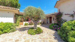 A courtyard with stone paving, a central tree, and surrounding greenery. - Villa Arasu - Private, gated estate 100 meters from the beach - Punta d'Araso (Zonza)