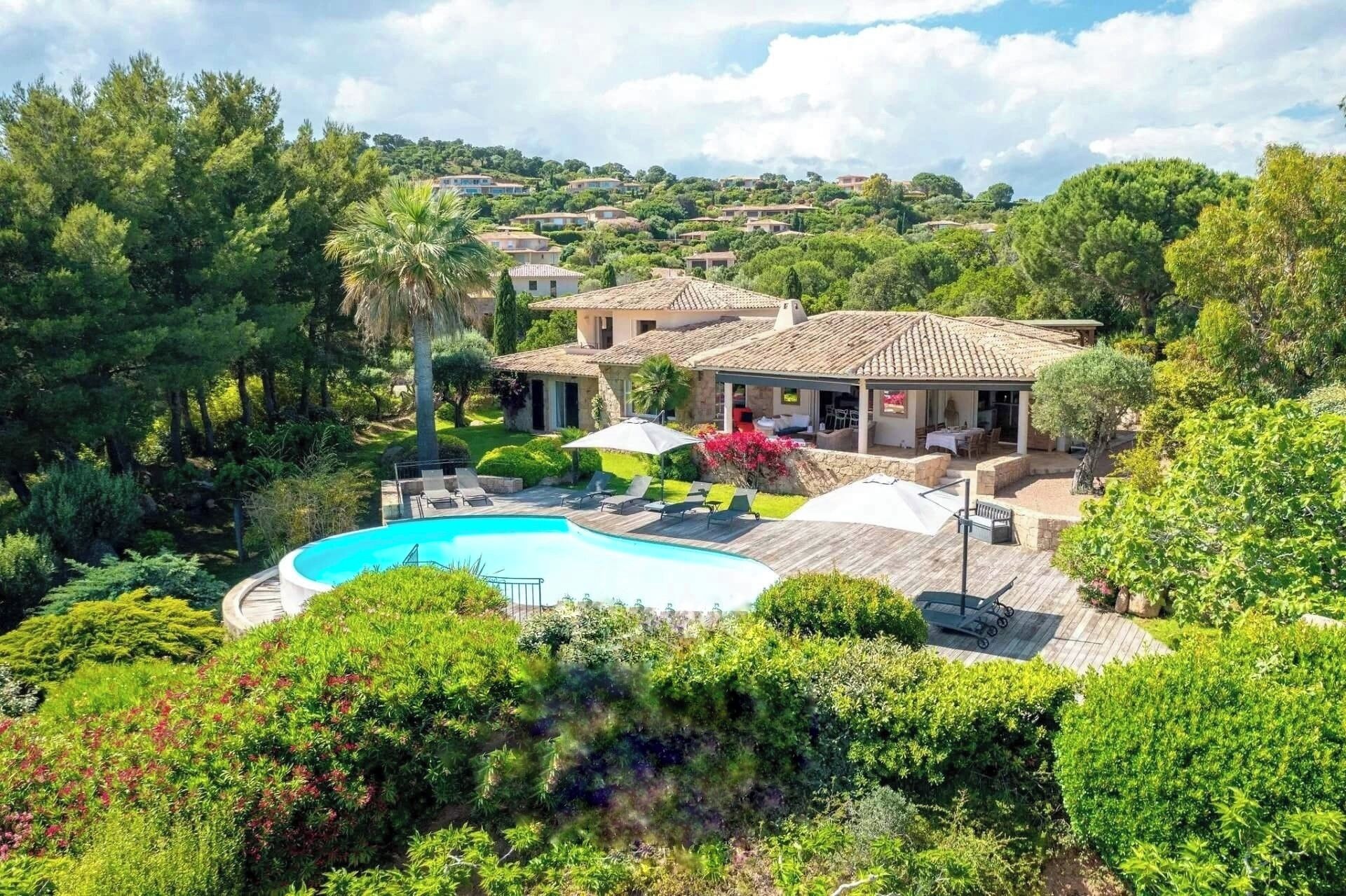 A villa with a swimming pool, outdoor seating, and a view of surrounding houses.