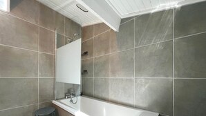 A modern bathroom with a large bathtub, a mirror, and a small stool. - RIVÉA - 2-bedroom apartment near the ocean (Mimizan)