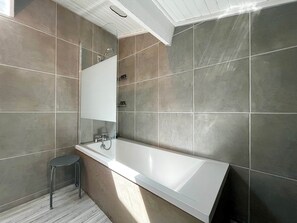 Ein modernes Badezimmer mit einer großen Badewanne, einem Spiegel und einem kleinen Hocker.