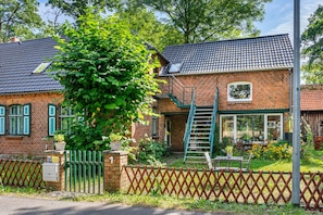 A brick house with a tiled roof, a green fence, and a ladder leading to the window.