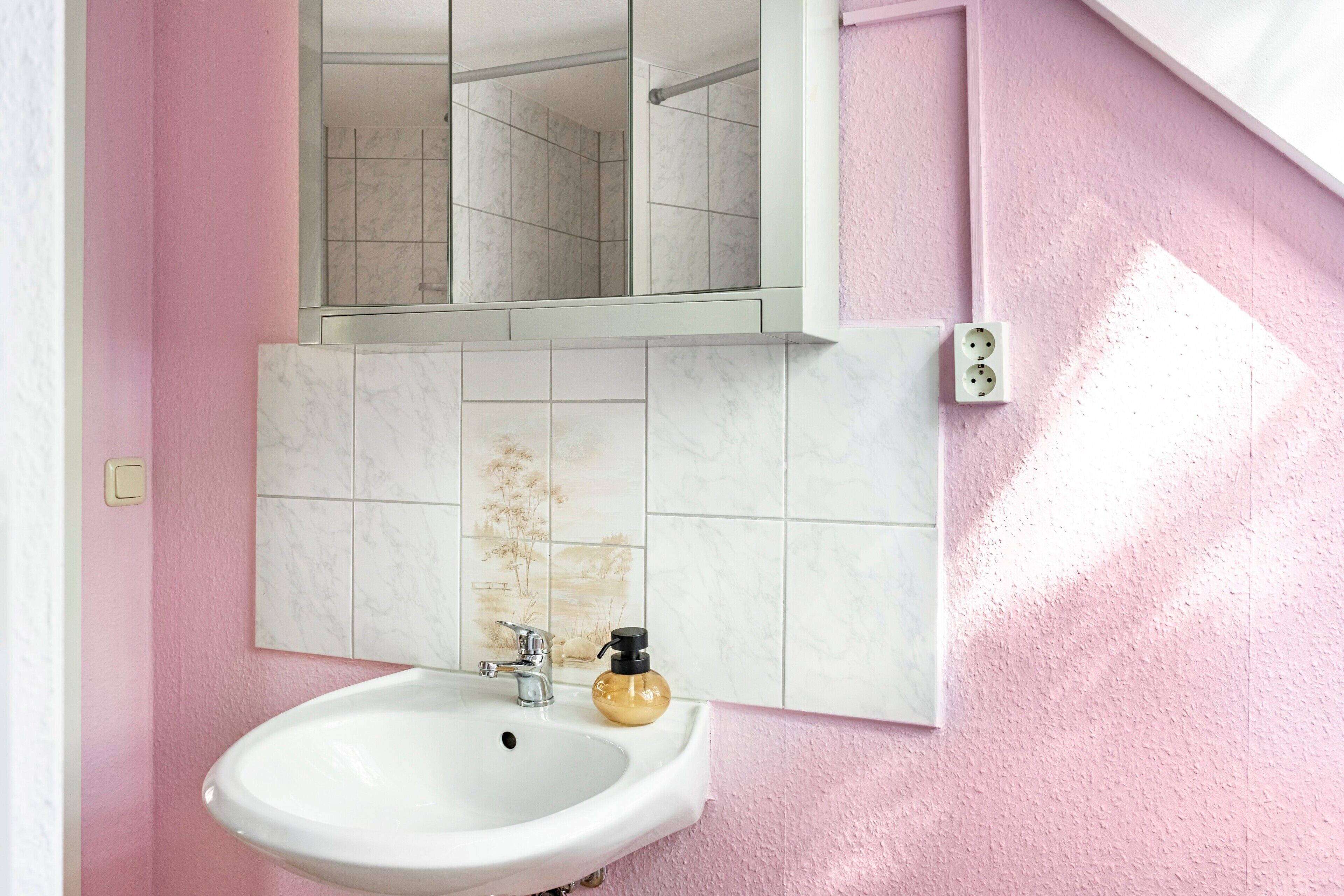 Een badkamer met een wit wastafelmeubel, een spiegel erboven en een roze wand.