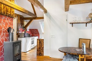 Ett kompakt kök med en vedspis, en mikrovågsugn och en liten ugn. Här finns också en matplats med ett runt bord och en stol.