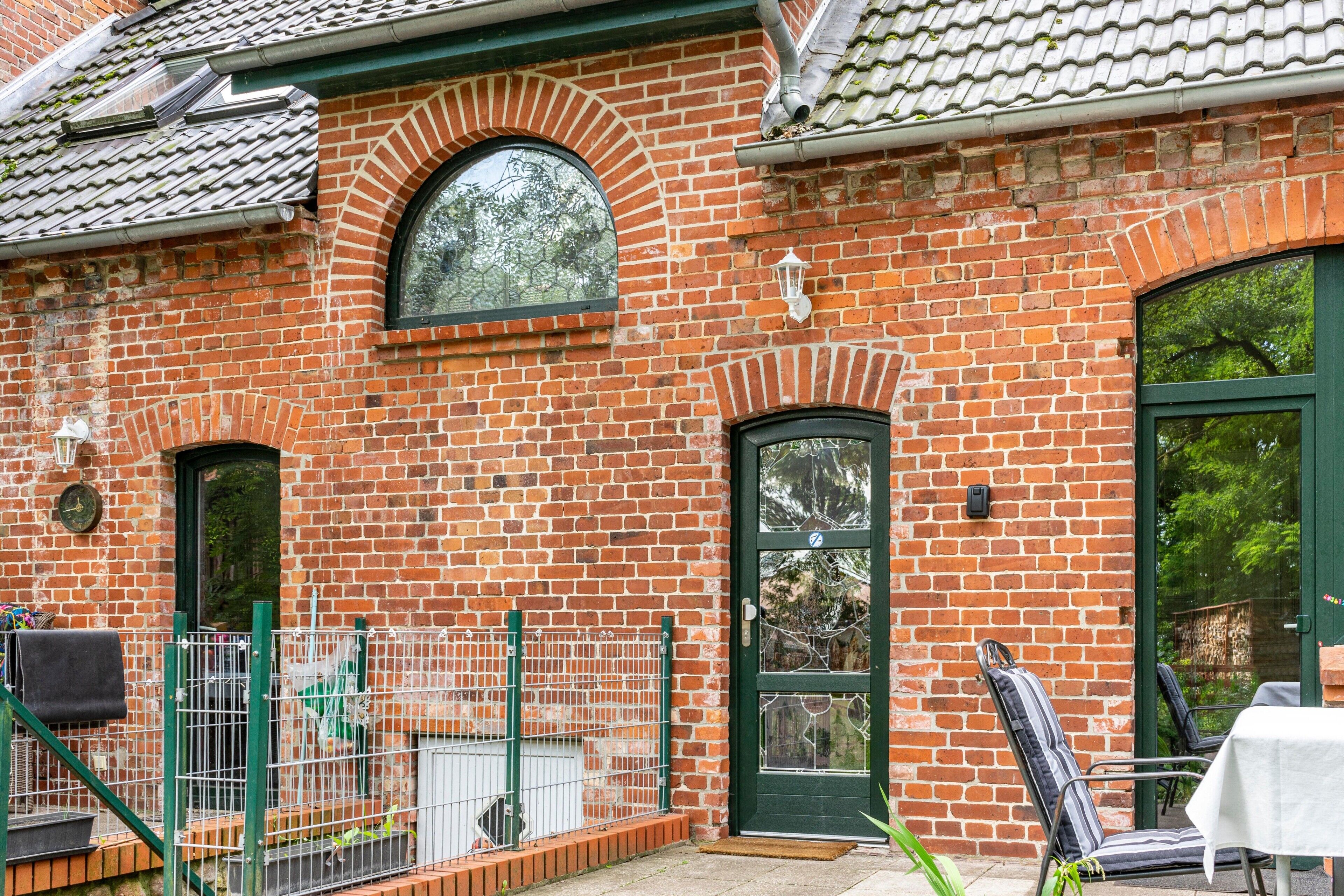 Een gebouw van baksteen met een groene deur, een raam en een klein terras met een tafel en stoelen.