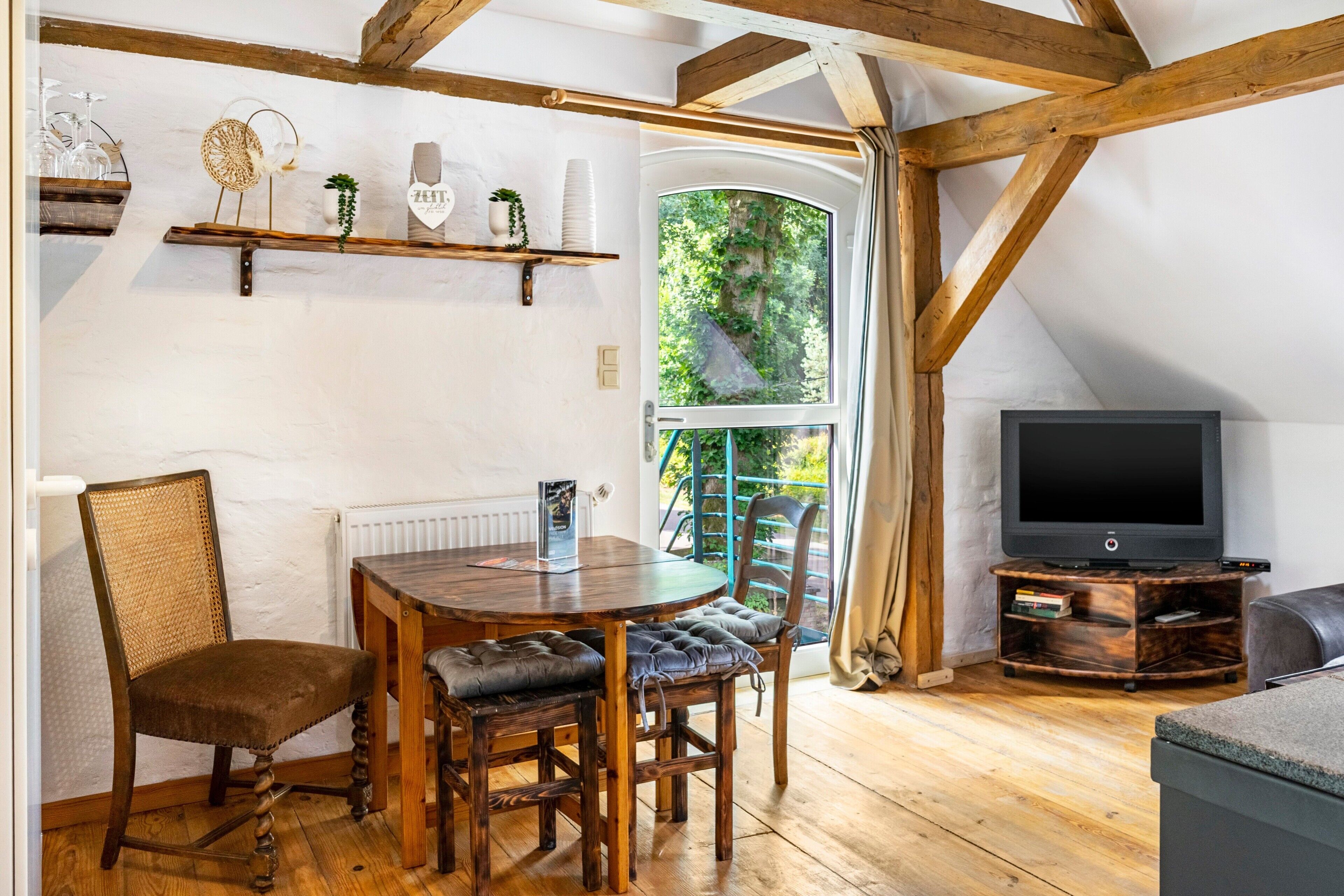 Ein gemütliches Zimmer mit einem Holzespeisetisch, Stühlen, einem Fernseher und einem Fenster mit Blick auf Grünflächen.
