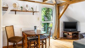 A cozy room with a wooden dining table, chairs, a television, and a window with a view of greenery.