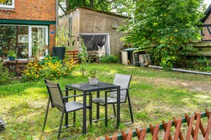 A garden with a table and chairs, a small shed, and a brick building with a window.
