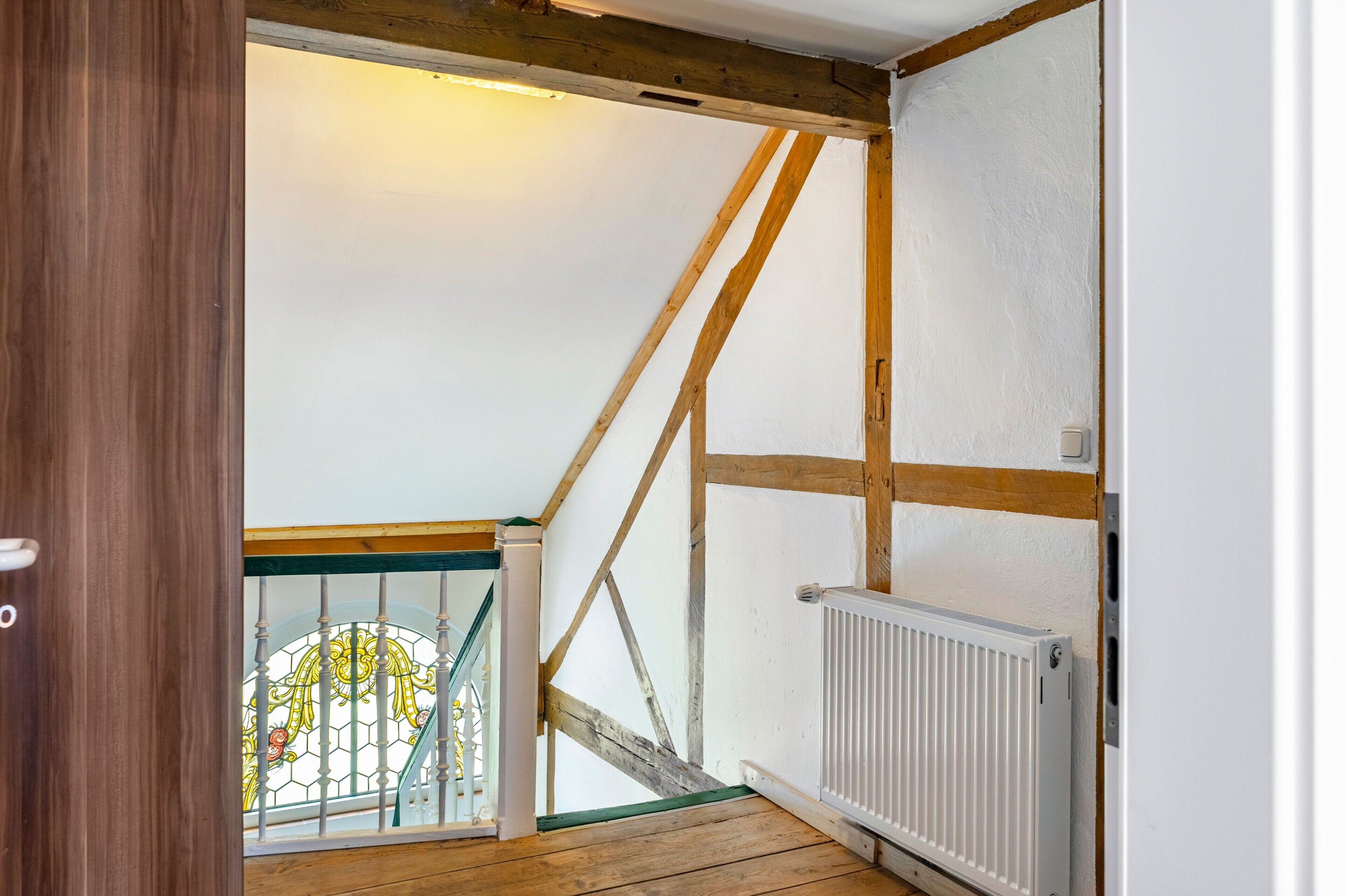 Ein Zimmer mit Holzboden, einem weißen Heizkörper und sichtbaren Holzbalken an der Decke.
