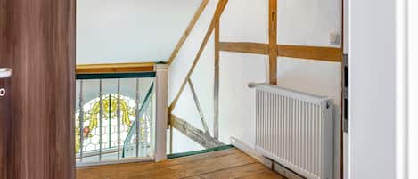 A room with a wooden floor, a white radiator, and a wooden ceiling beam structure.