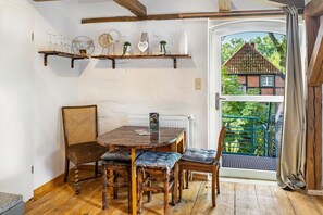 Área de refeições com mesa de madeira, cadeiras e vista para uma casa através de uma porta de vidro.